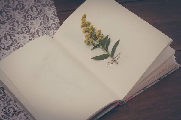 A high angle shot of a nice flower taped to the sheet of a notebook on a wooden table - Zdjęcie, obraz