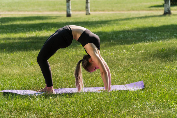 Una chica en ropa deportiva al aire libre hace un ejercicio para bajar de peso. Yoga, concepto de entrenamiento funcional utilizando una alfombra al atardecer
. - Foto, Imagen