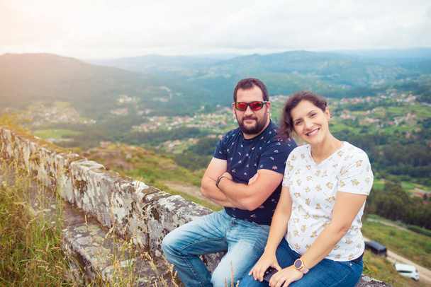Schwangere heterosexuelle Paare posieren vor einer wunderschönen Landschaft mit Bergen und Wäldern - Foto, Bild
