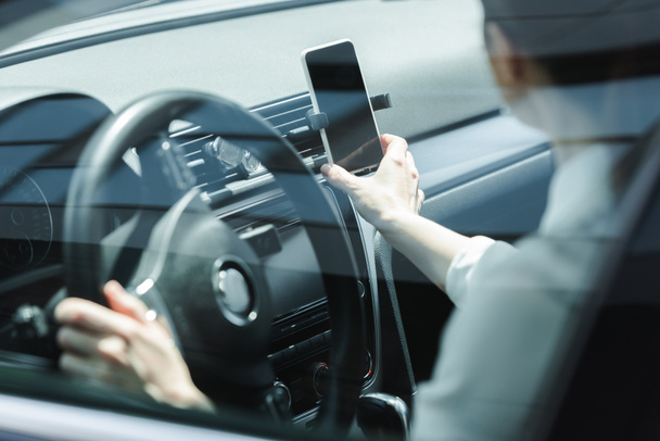 Enfoque selectivo de la mujer de negocios sosteniendo el teléfono inteligente mientras conduce el coche
  - Foto, imagen