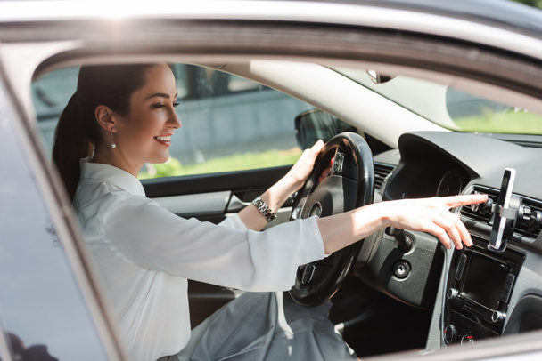 Side view of smiling businesswoman using smartphone while driving auto  - Foto, Imagen