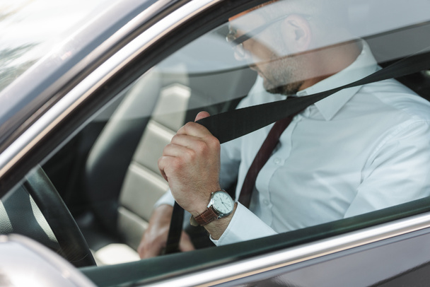Selective focus of businessman fastening seat belt in car  - Foto, imagen