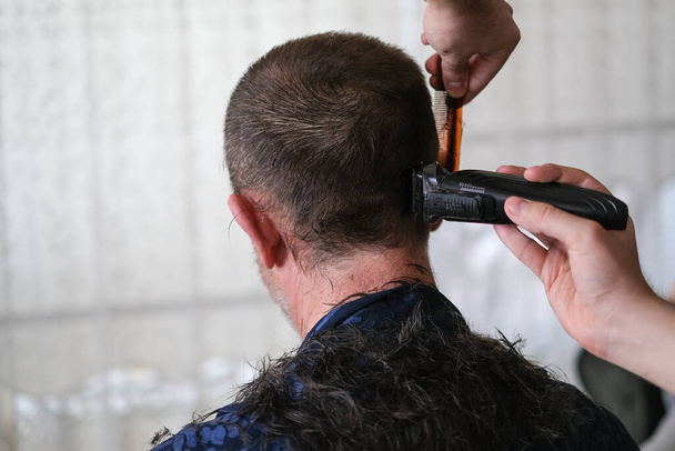 El joven está cortando el pelo del padre con la cortadora de pelo durante el aislamiento de cuarentena coronavirus en el hogar.
. - Foto, imagen
