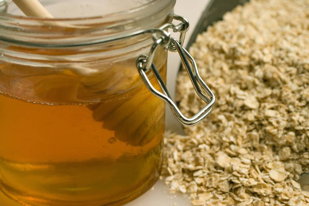 A closeup shot of honey in a jar and oats on the table - Foto, imagen