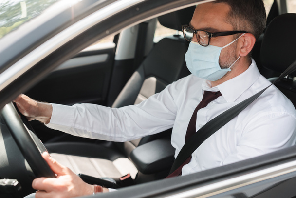 Selectieve focus van zakenman in medisch masker rijden auto  - Foto, afbeelding