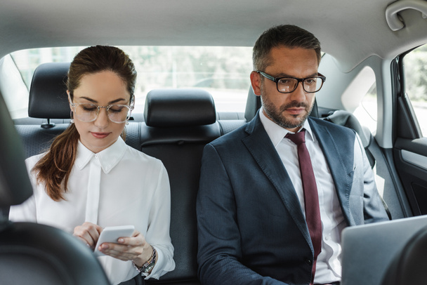Selective focus of business people using digital devices in car  - Foto, imagen