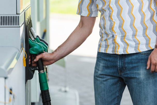 Vista cortada do homem segurando o bico de abastecimento no posto de gasolina ao ar livre
  - Foto, Imagem