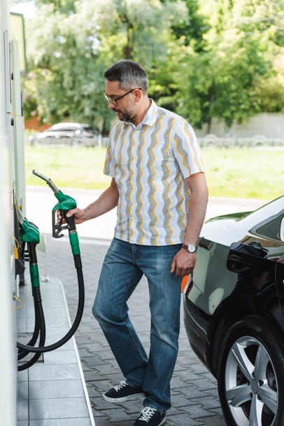 Focus selettivo dell'uomo che tiene l'ugello di rifornimento sul distributore di benzina vicino all'auto sulla strada urbana  - Foto, immagini