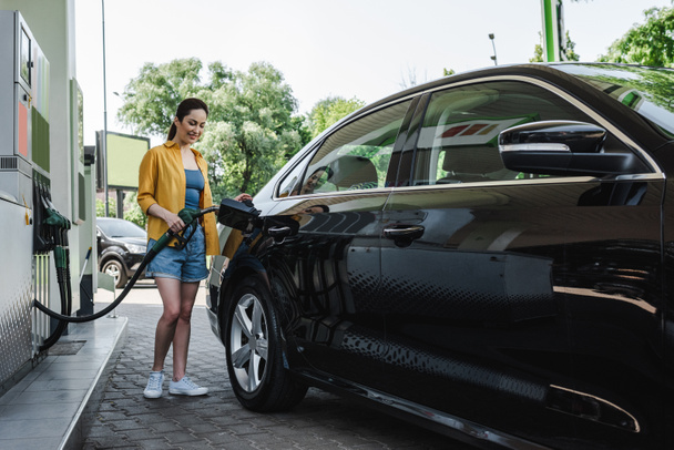 Piękna uśmiechnięta kobieta tankuje samochód na stacji benzynowej  - Zdjęcie, obraz