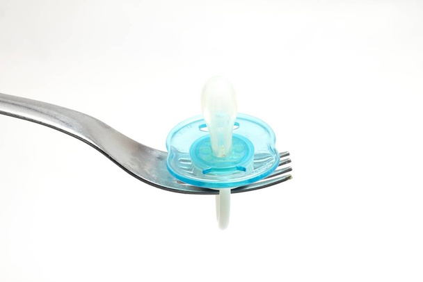 A closeup shot of a blue pacifier on a fork isolated on white background - Fotó, kép