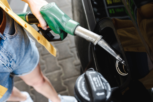 Cropped view of woman holding fueling nozzle near car on gas station - Photo, Image