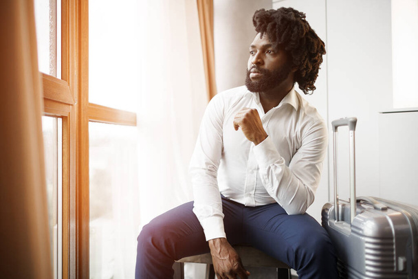 Black man businessman sitting and looking at window in hotel room - Фото, зображення