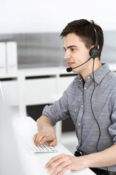 Casual dressed young man using headset and computer while talking with customers online. Call center, business concept - Foto, immagini