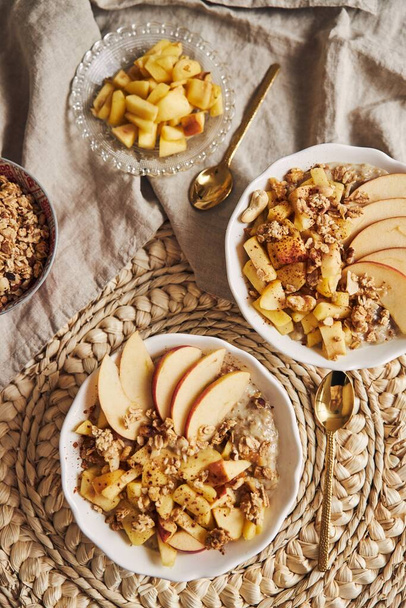 A vertical high angle shot of a bowl Porridge with cereal and nuts, and slices of apple on a table - Photo, Image