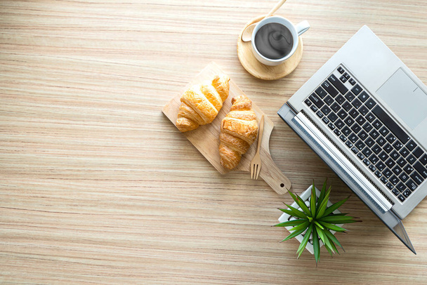 Overhead shot of modern office room with laptop computer, coffee cup, croissant on table background - Foto, Imagem