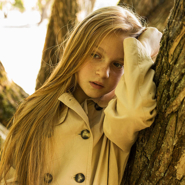 公園の木の幹樹皮の木々の間に長い髪とそばかすを持つ美しい赤い髪の少女の肖像画10-12歳。自然との統一。エコライフ。夏休み - 写真・画像