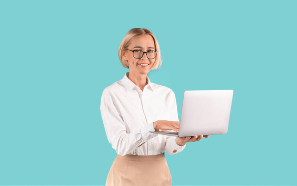 Femme d'affaires confiante avec ordinateur portable souriant sur fond bleu - Photo, image