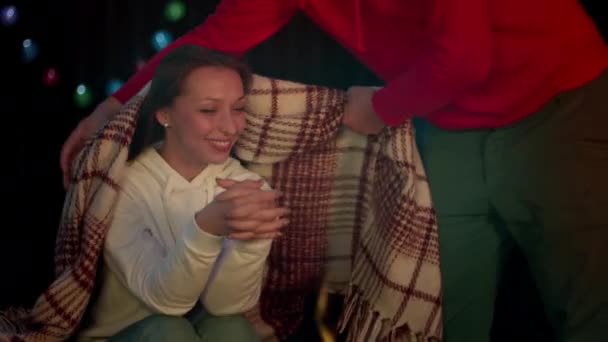 Man covers girl with plaid and sits down. Romantic evening near bonfire - Felvétel, videó