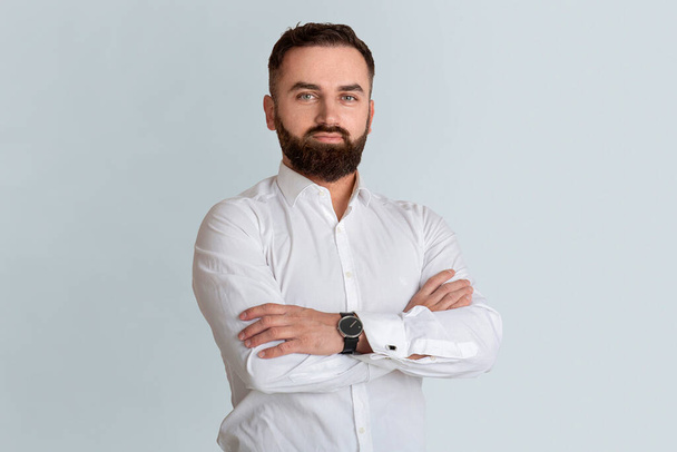Attractive bearded CEO in white shirt standing with crossed arms on grey background - Photo, Image