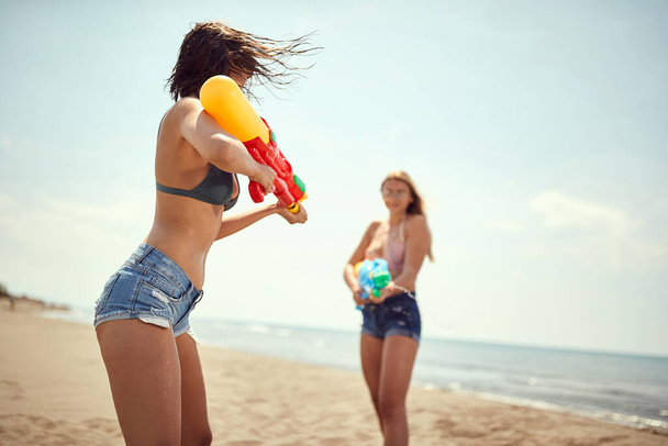 two caucasian women playing with water-guns on sandy beach - 写真・画像
