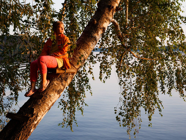 hermosa chica en un árbol sobre el agua al atardecer 2020
 - Foto, Imagen