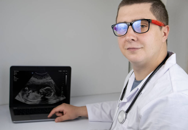Ein Gynäkologe untersucht das Ergebnis einer Ultraschalluntersuchung des Fötus auf einem Computermonitor. Schwangerschaftsmanagement-Konzept - Foto, Bild