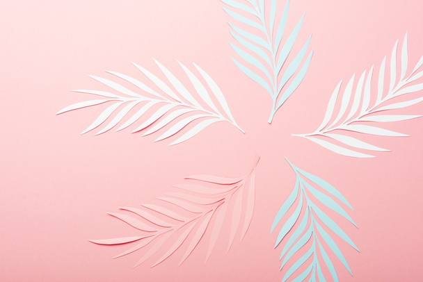 bovenaanzicht van wit, roze en blauw papier gesneden palmbladeren op roze achtergrond - Foto, afbeelding