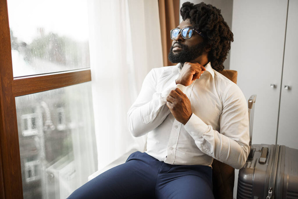 Homem negro homem de negócios sentado e olhando para a janela no quarto de hotel
 - Foto, Imagem