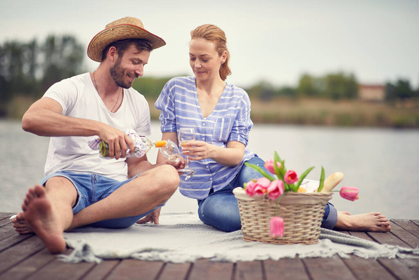 Молодая улыбающаяся пара празднует с вином на пикнике
 - Фото, изображение