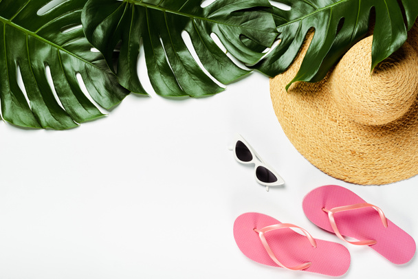 vue du dessus des feuilles de palmier vert, chapeau de paille, lunettes de soleil et tongs sur fond blanc - Photo, image