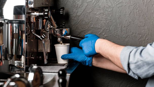 Καφέ και καραντίνα. Barista σε λαστιχένια γάντια κάνει καπουτσίνο με μηχανή καφέ - Φωτογραφία, εικόνα