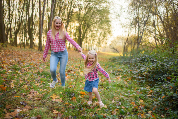 Moeder en dochter in jeans en roze shirts lopen in het najaarspark. - Foto, afbeelding