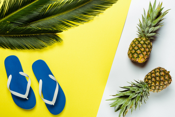 top view of green palm leaves, pineapples and blue flip flops on white and yellow background - Photo, Image