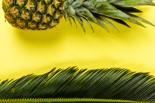 top view of green palm leaf and ripe pineapple on yellow background - Fotó, kép