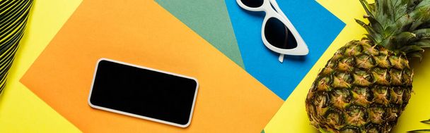 horní pohled na sluneční brýle, smartphone a zralé ananas na barevném pozadí, panoramatický záběr - Fotografie, Obrázek