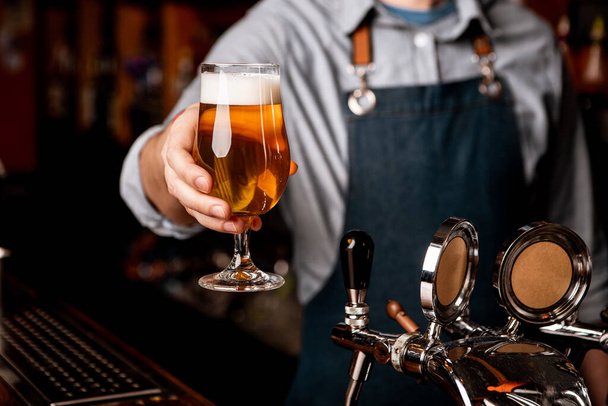 Birra venerdi 'sera. Barman dà vetro di birra leggera con schiuma in interni scuri - Foto, immagini