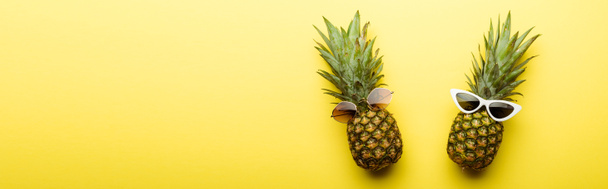 top view of ripe pineapples in sunglasses on yellow background, panoramic shot - Фото, изображение