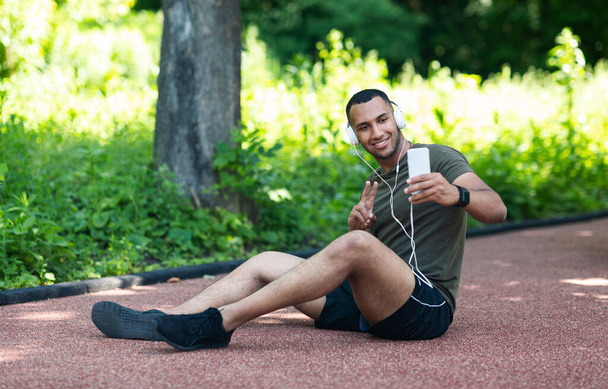 Afrikai amerikai futó szelfit készít, miközben pihen edzés után a parkban. - Fotó, kép