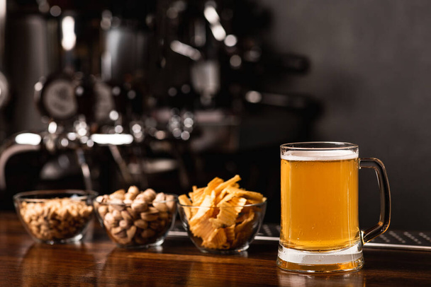 Ambachtelijk bier festival. Pistaches, chips en noten in glazen borden en bier in mok in interieur - Foto, afbeelding