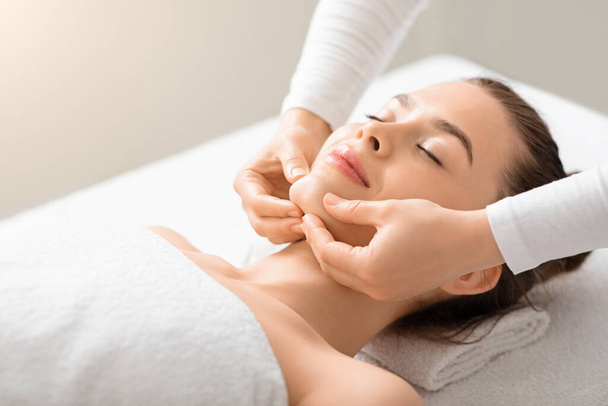 Relaxed young lady having lifting face massage at spa - Photo, Image