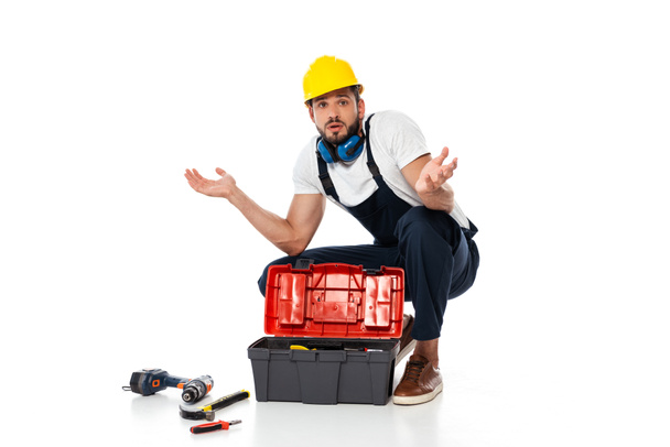 Confused workman showing shrug gesture near tools and toolbox on on white background - Photo, Image