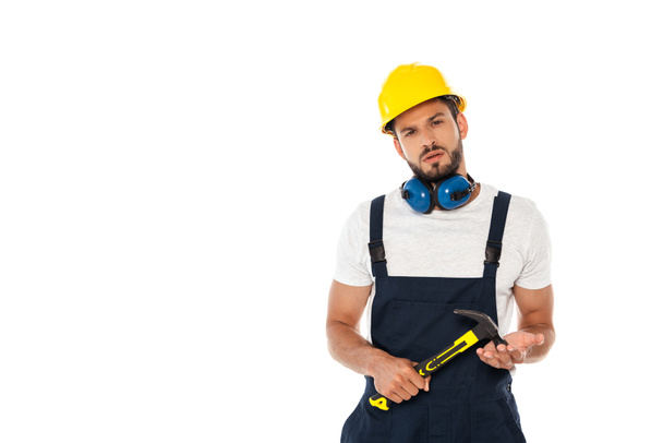 Handsome workman in uniform and hardhat holding hammer and looking at camera isolated on white - Photo, Image