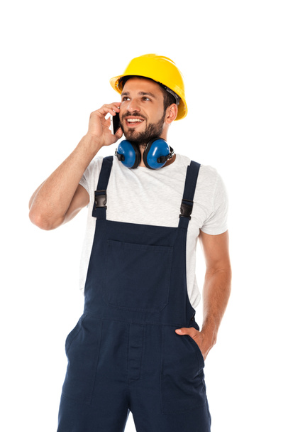 Glimlachende reparateur in overalls praten op smartphone geïsoleerd op wit - Foto, afbeelding