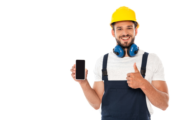 Smiling handyman in workwear showing like gesture while holding smartphone with blank screen isolated on white - Photo, Image