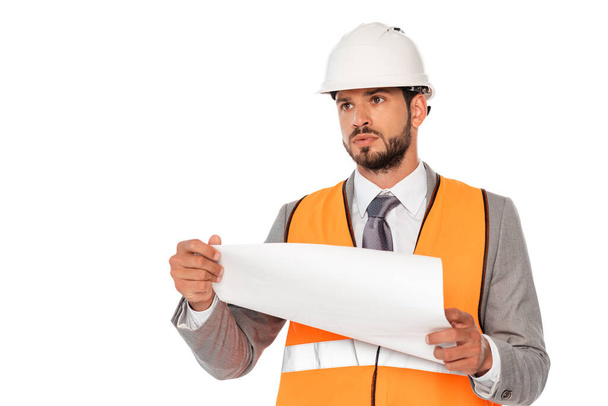 Handsome engineer in suit and hardhat holding blueprint and looking away isolated on white - Fotó, kép