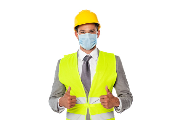 Mérnök keménykalapban és orvosi maszkban, hüvelykujját fehér alapon elszigetelve mutatja. - Fotó, kép