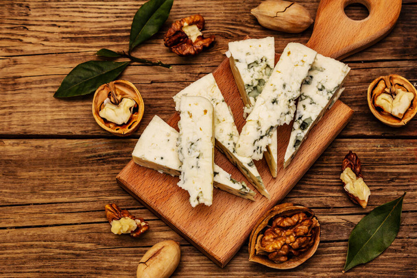 青カビチーズ。チーズプレートの材料。ナッツ、香りの良いベイリーフ、ナイフ。ヴィンテージ木製ボードの背景を閉じます - 写真・画像