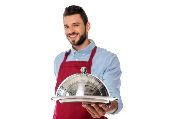 Выборочный фокус улыбающегося бородатого официанта, держащего поднос и клош изолированный на белом
 - Фото, изображение