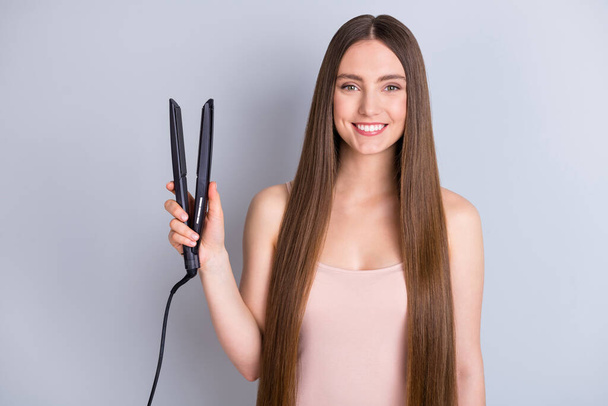 Photo of beautiful model lady demonstrating long hairstyle hold electric styler curler straight curls ready for romantic date wear beige singlet isolated grey color background - Photo, Image