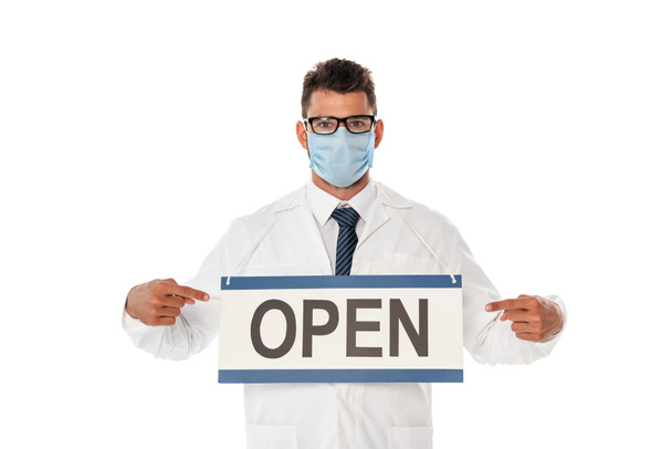 Doctor in medical mask pointing with fingers at signboard with open lettering isolated on white - Foto, imagen